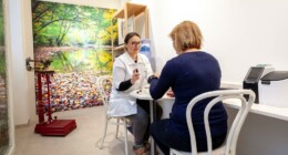 Auf dem Bild, macht eine Mitarbeiterin der Apotheke eine Beratung. Sie hat ein Fläschen in der Hand