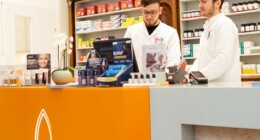 Zwei männliche Mitarbeiter der Dreifaltigkeits Apotheke stehen hinter dem Verkaufspult