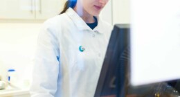 Auf dem Bild: eine junge Mitarbeiterin der Dreifaltigkeits Apotheke, hinter einem Monitor stehend